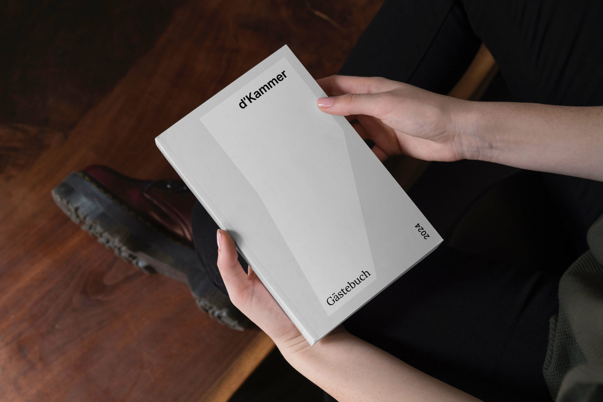 Frau hält Gästebuch über d'Kammer in der Hand. Logo in weiß, Hintergrund in grau.