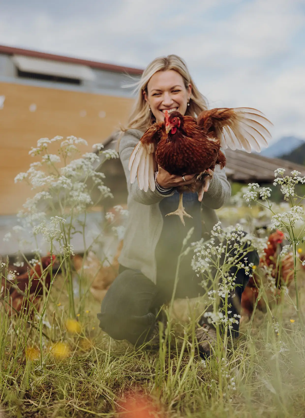 Eine junge blonde Frau hält ein Huhn in der Hand, das gerade davon fliegt.