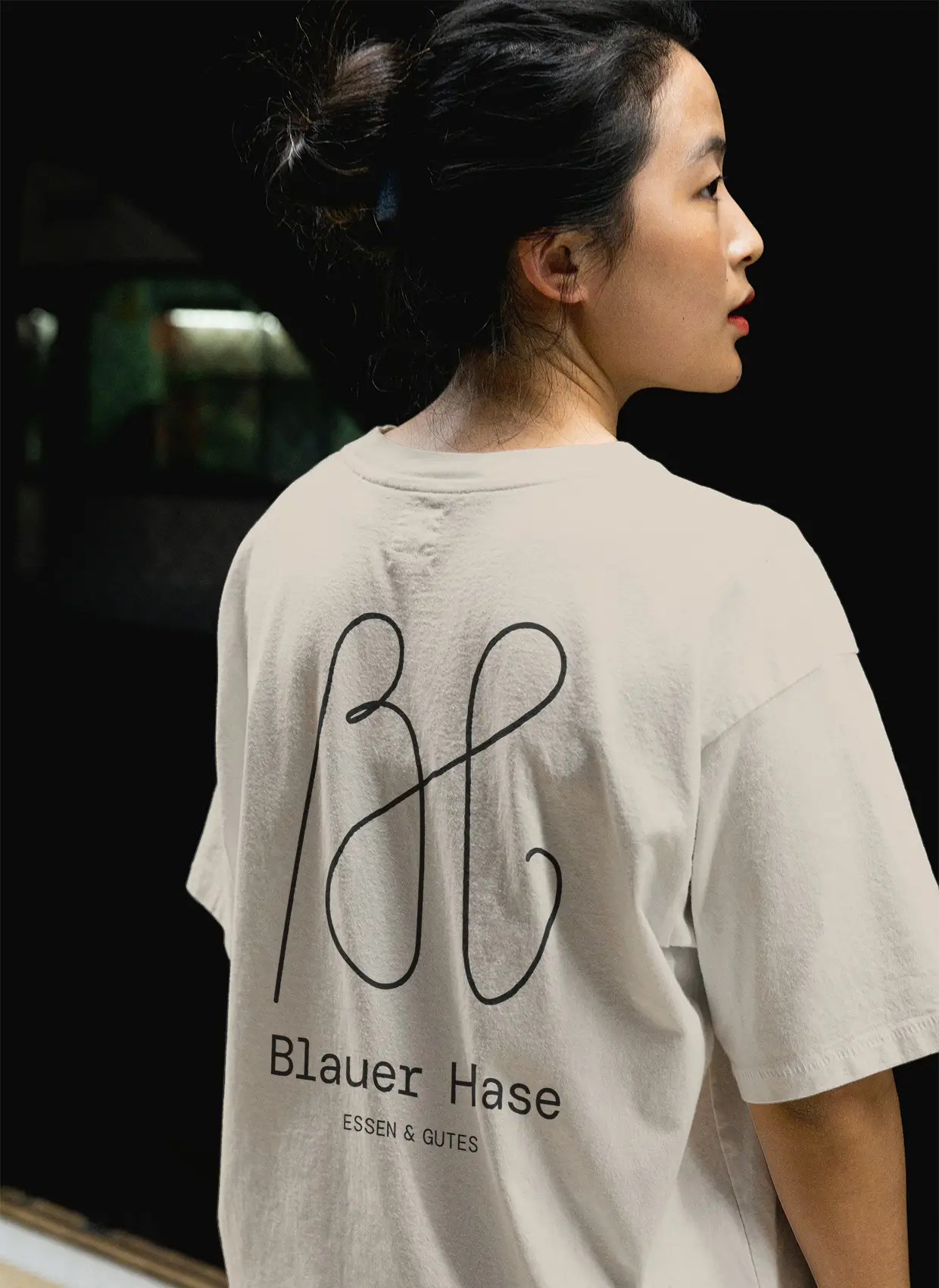 Frau von hinten mit Blick über Schulter, beiges T-Shirt mit schwarzem Blauer Hase Logo