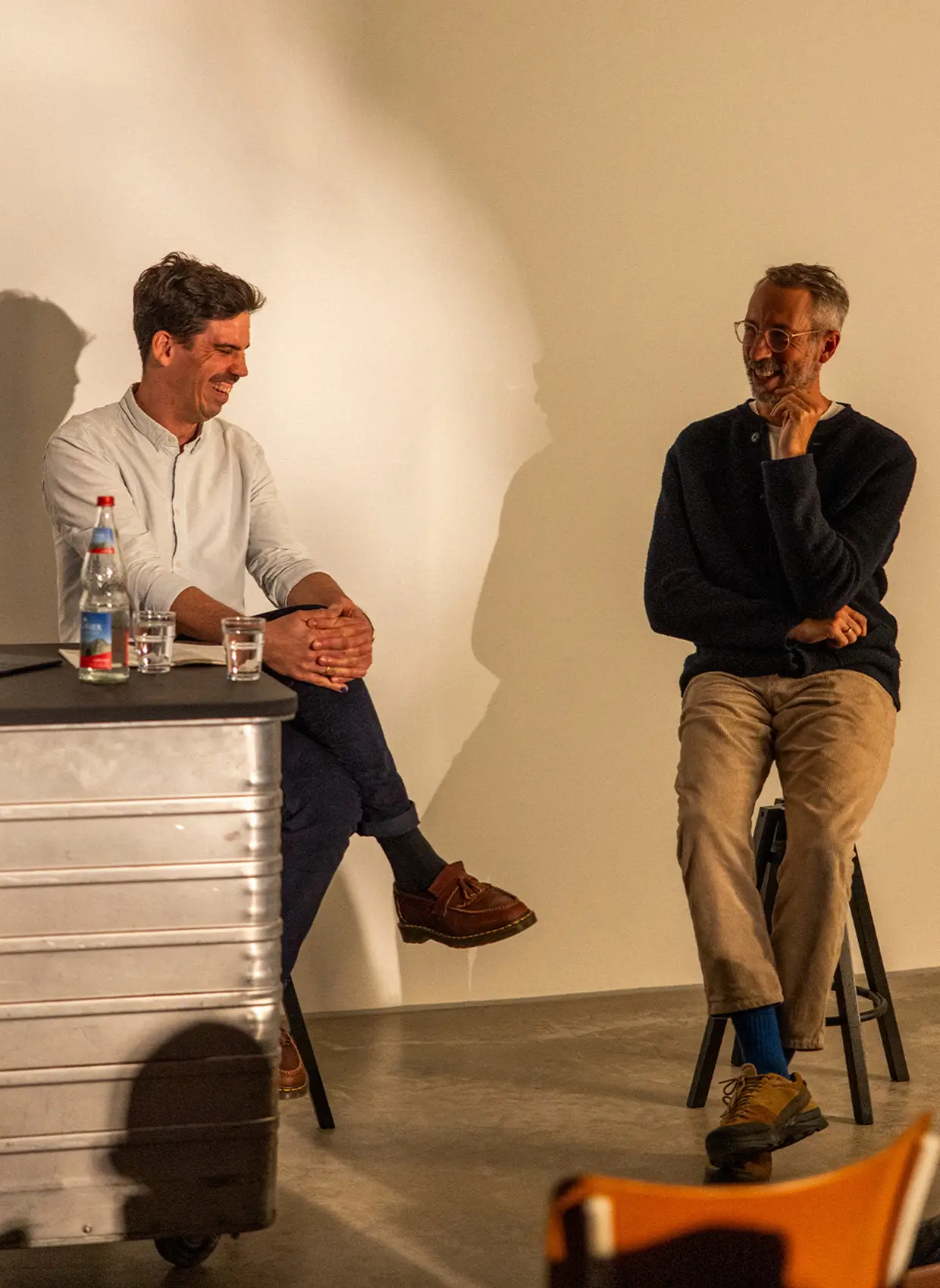 Zwei Männer, auf Hockern sitzend, unterhalten sich vor Publikum