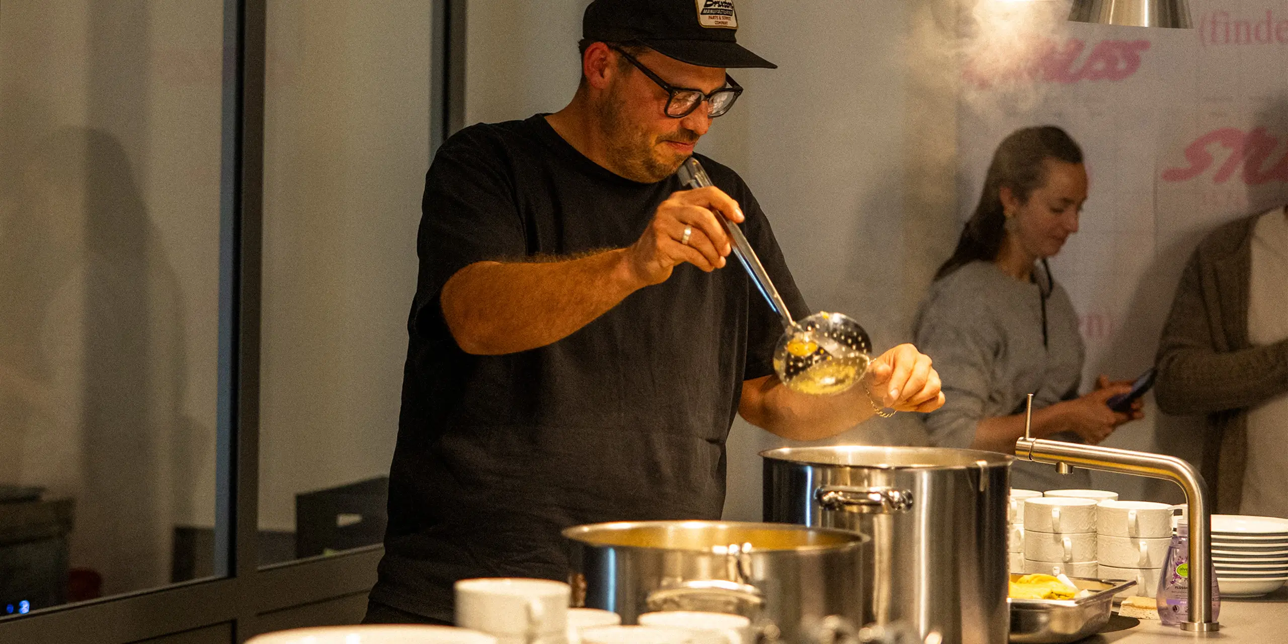 Mann rührt Suppe in einem großen Topf hinter einer Theke